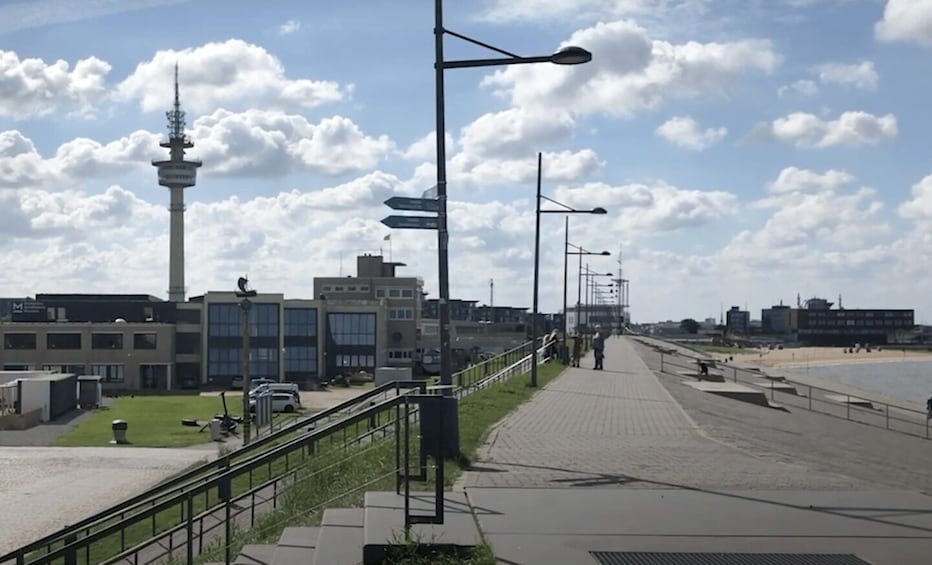 A coastal promenade with a tower, buildings, and a beach. 2