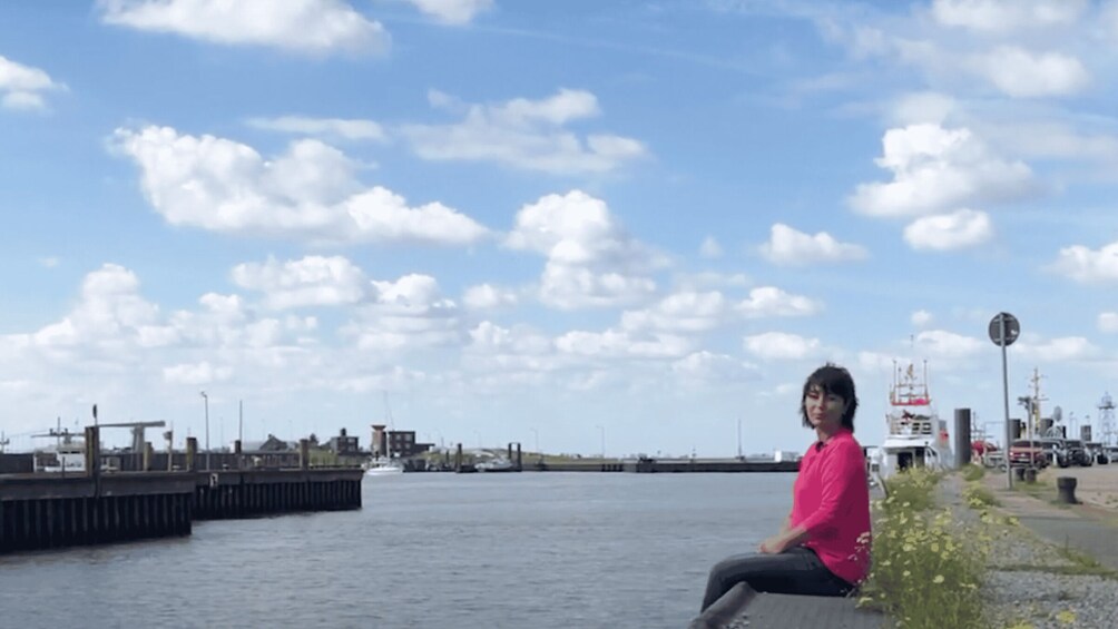 A person sitting by a waterfront with a dock and boats in the background. 4