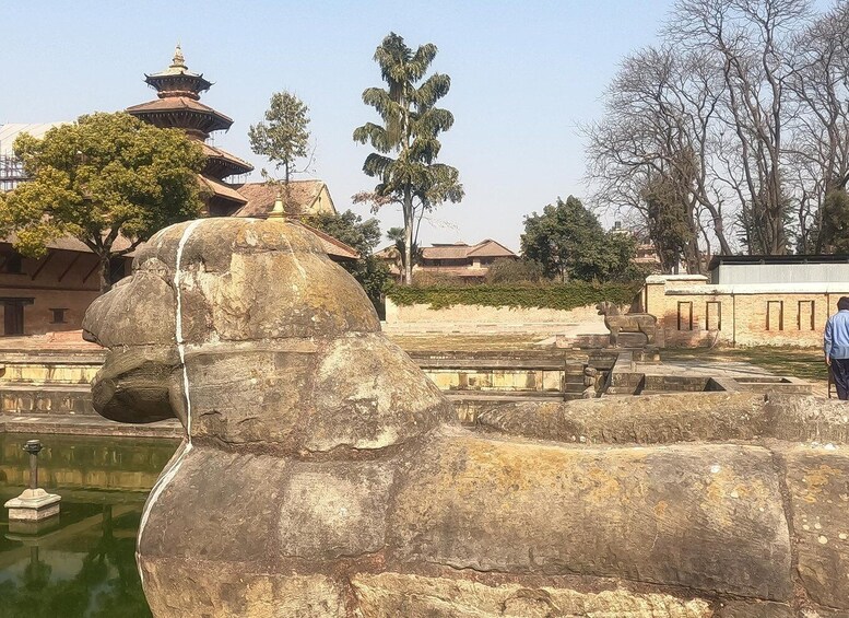 A large stone elephant sculpture in a courtyard with a pond, surrounded by trees and traditional buildings. 2