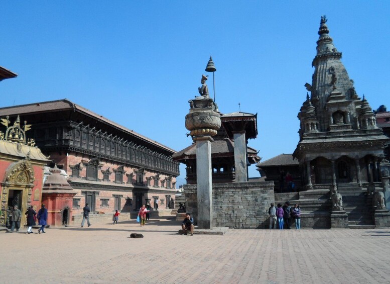 A historical building with traditional architecture, a stone pillar with a statue, and a large stupa. 1