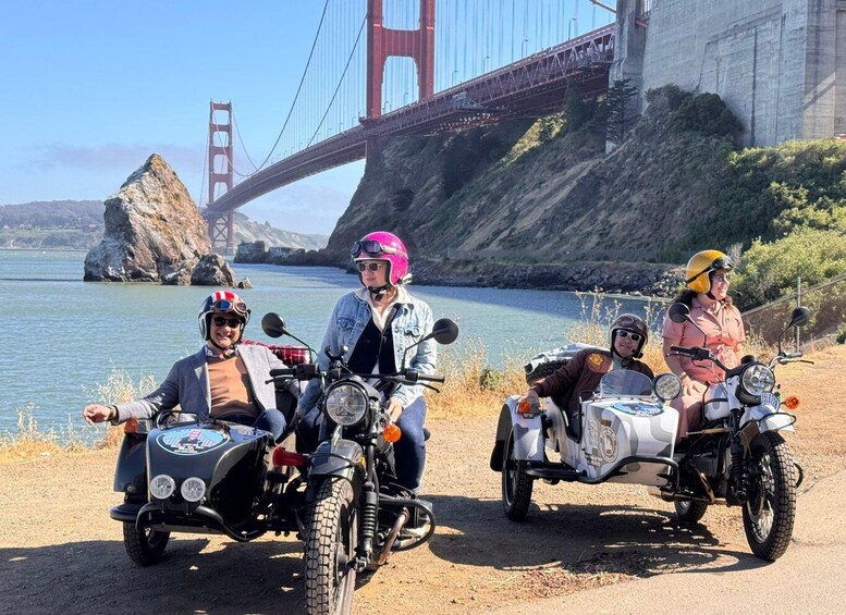 A group of people on motorcycles by a body of water with a bridge in the background. 1