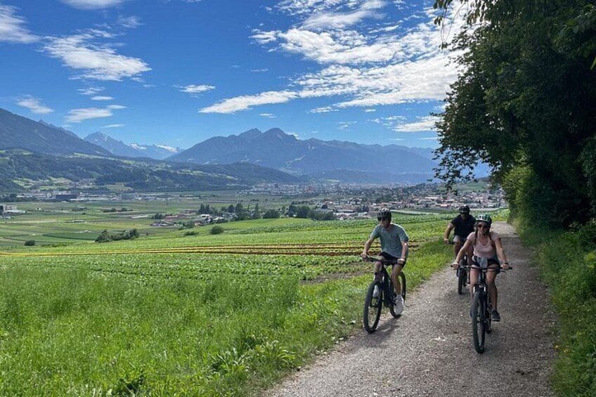 Ciclistas en un sendero de grava con paisaje rural, campos y montañas al fondo. 3