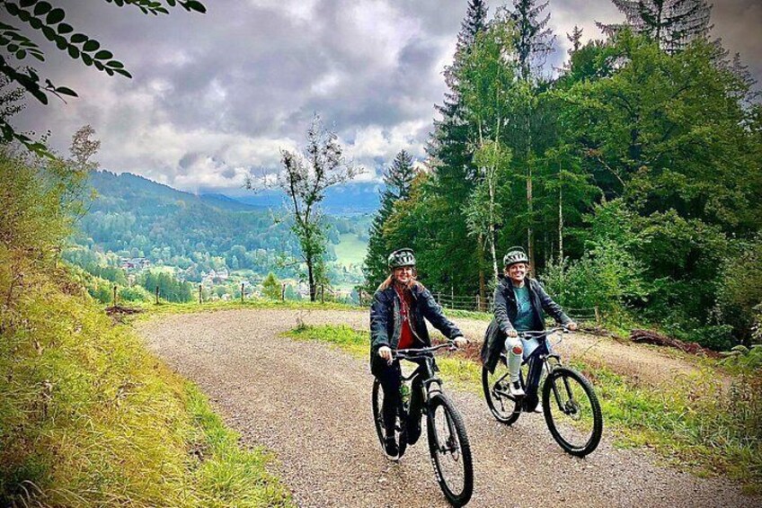 Dos ciclistas en un camino de grava rodeados de árboles y montañas. 5