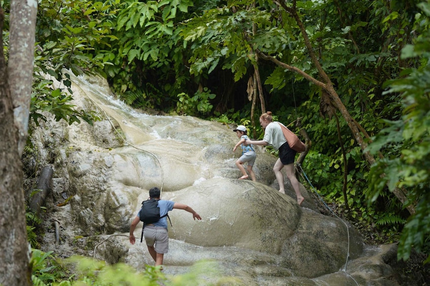 People hiking on a rocky waterfall in a forested area. 1