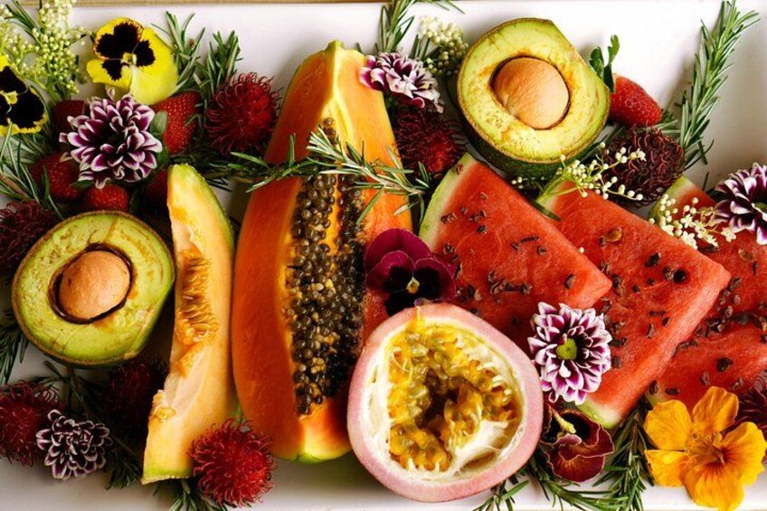 A variety of fruits and flowers, including papaya, watermelon, and passion fruit, arranged on a white surface. 2