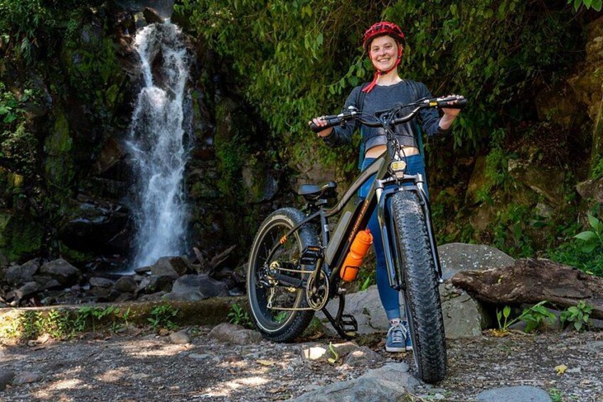 A person standing next to a mountain bike with a waterfall in the background. 4