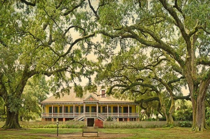Een historisch gebouw met een veranda, omgeven door grote bomen. 1