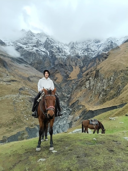A person riding a horse on a grassy hillside with a mountainous backdrop. 2