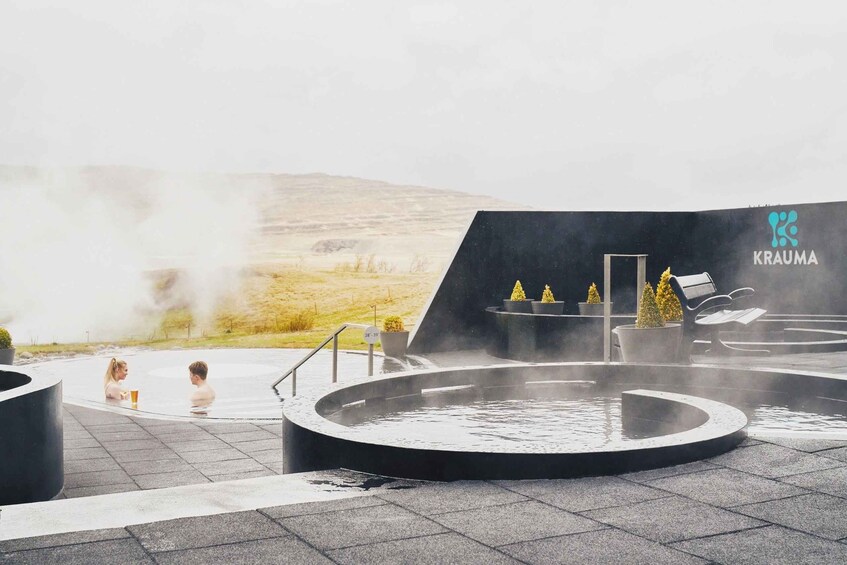Un spa geotérmico con una piscina caliente circular, zonas de estar y el logo de 'KRAUMA' al fondo. 1