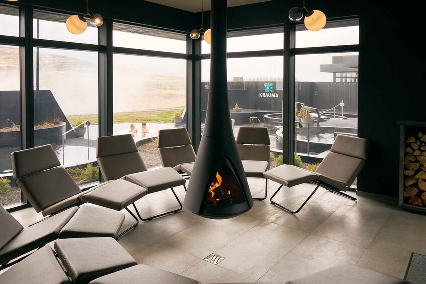 Un salón moderno con una chimenea central, ventanas amplias y asientos exteriores. 5