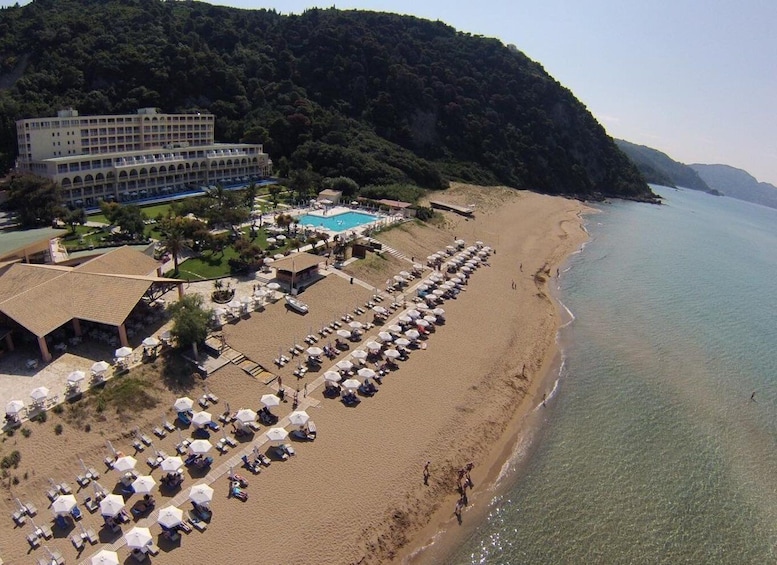A beach with sun loungers and umbrellas, a swimming pool, and a hotel. 2