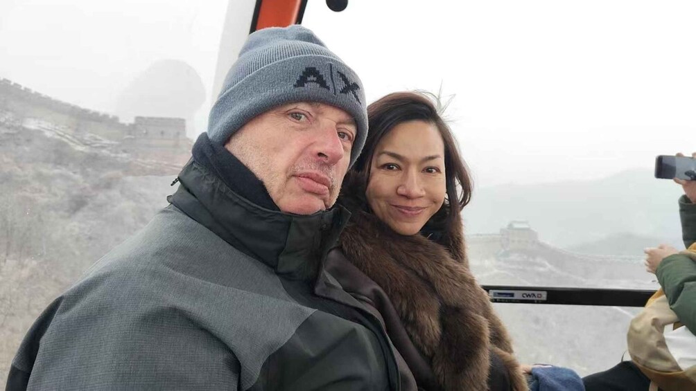 A person in a grey jacket and a person in a brown coat sitting in a vehicle with a mountainous landscape in the background. 5