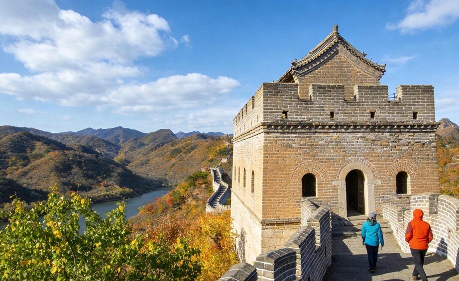 A stone wall with a traditional roof, overlooking a valley with a river and mountains. 1