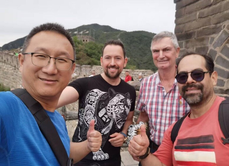 Four people posing in front of a historical site with stone walls and a mountainous background. 2