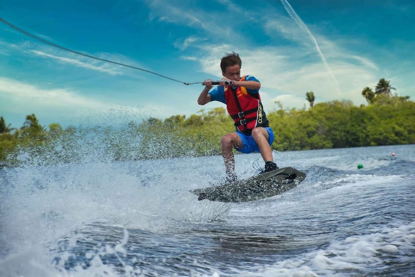 Una persona practica wakeboard en un cuerpo de agua, con árboles al fondo. 5