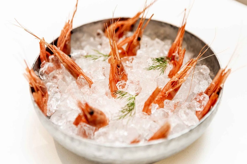 A bowl of cooked shrimp on ice with a sprig of dill. 1
