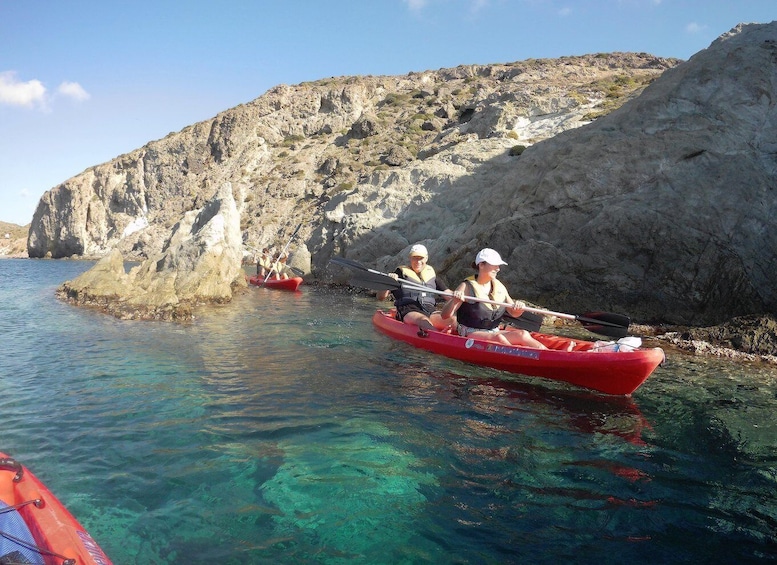 Two people kayaking in clear water near rocky cliffs. 2