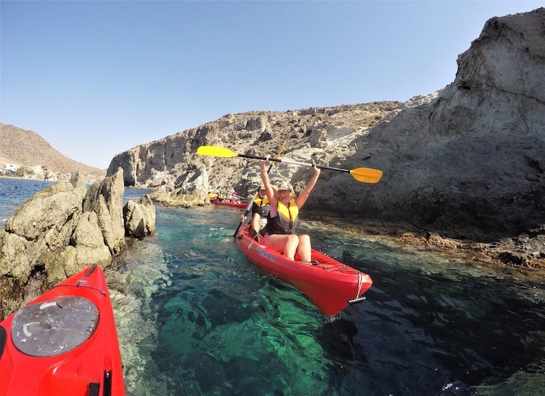 A person kayaking on clear water with rocky cliffs in the background. 1