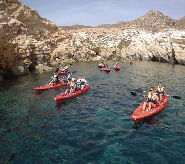 People kayaking in a clear, rocky cove surrounded by mountains. 3