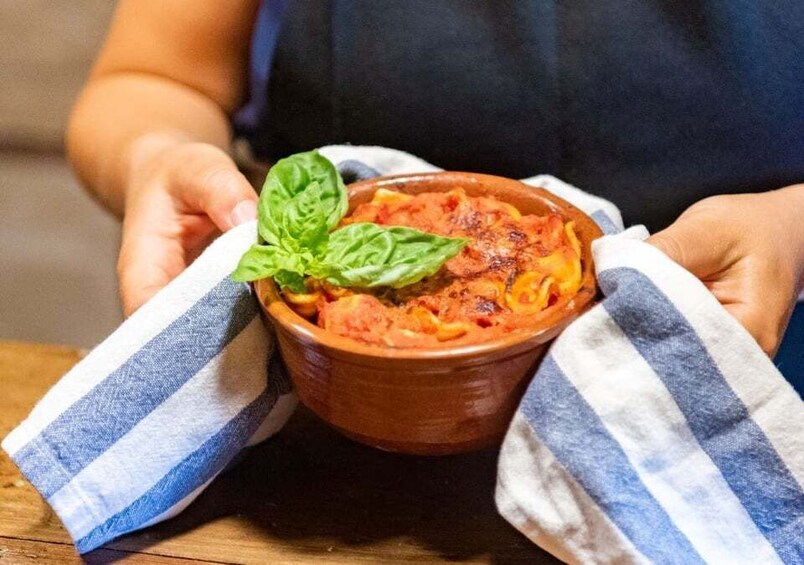 A person holding a bowl of food with a basil leaf on top. 1