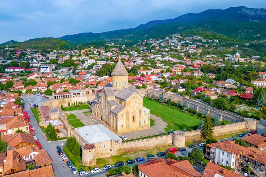 Un pueblo histórico con una iglesia destacada rodeada por una muralla, sobre un paisaje de colinas ondulantes y un cielo despejado. 2