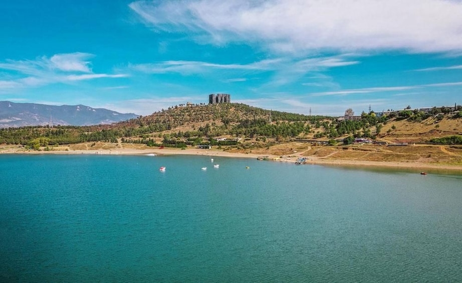 Un lago con barcos, una colina con edificios y montañas al fondo. 3