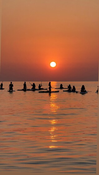 Un atardecer sobre un mar tranquilo con gente haciendo paddleboard. 4