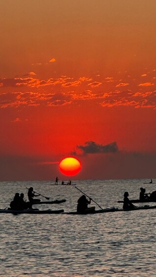 Un atardecer sobre un cuerpo de agua con gente en canoas. 3