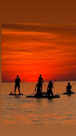Un atardecer sobre el agua con gente haciendo paddleboard. 2