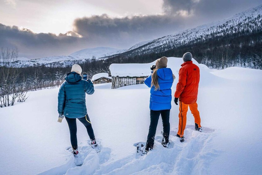 Three people standing on a snowy mountain, looking at a cabin in the distance. 4