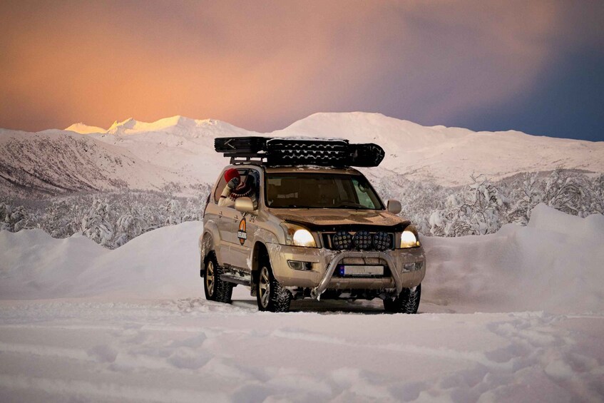 A snow-covered SUV with a roof rack and off-road tires, parked on a snowy mountain. 2