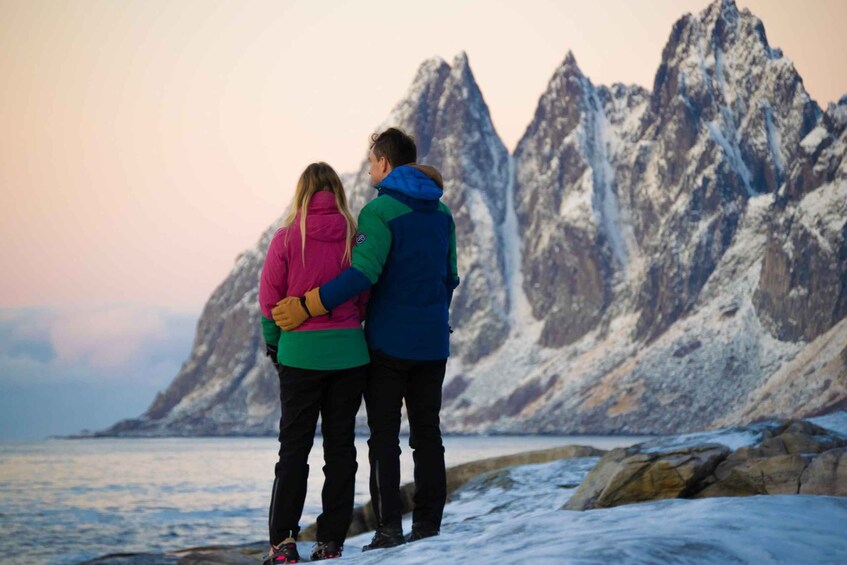 Two people standing on a rocky shore with a mountainous backdrop. 3