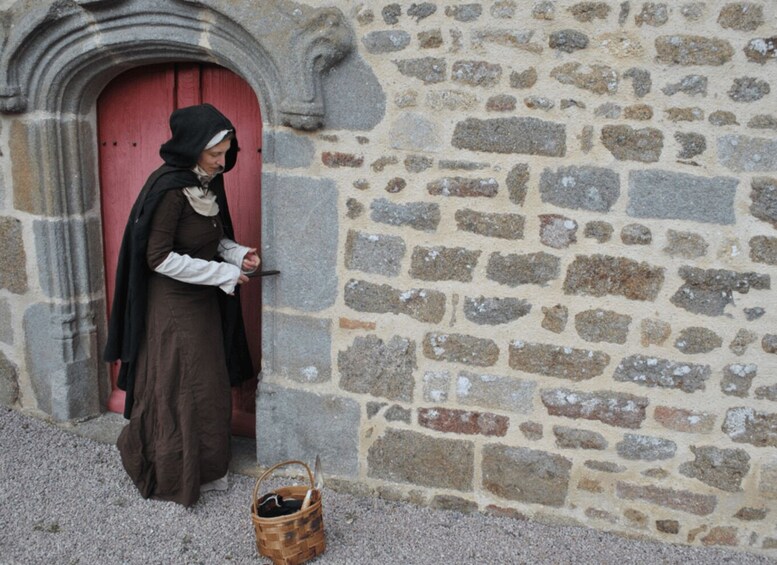 A person in historical clothing standing at a stone building entrance with a red door. 2