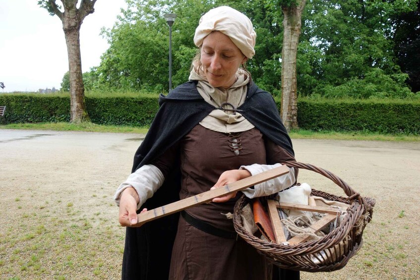A person in historical costume holding a long wooden object and a basket with various items. 4