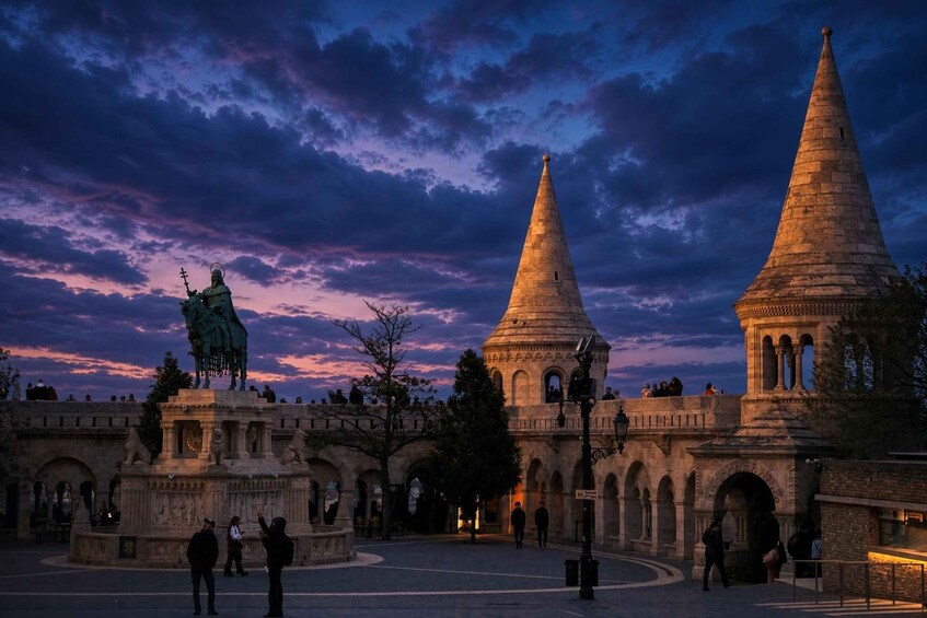 A historical square with a statue, two prominent towers, and an ornate building with arches. 3