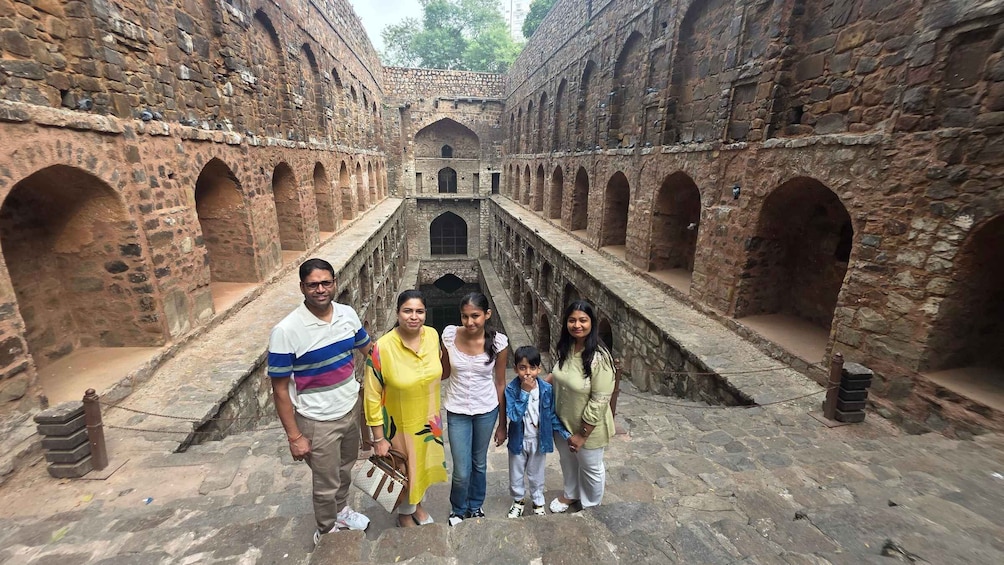 A group of people standing in an ancient stone courtyard with arches and a central staircase. 1