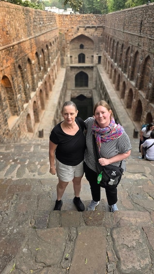 Two people standing on a stone pathway with a historical building featuring arches in the background. 5
