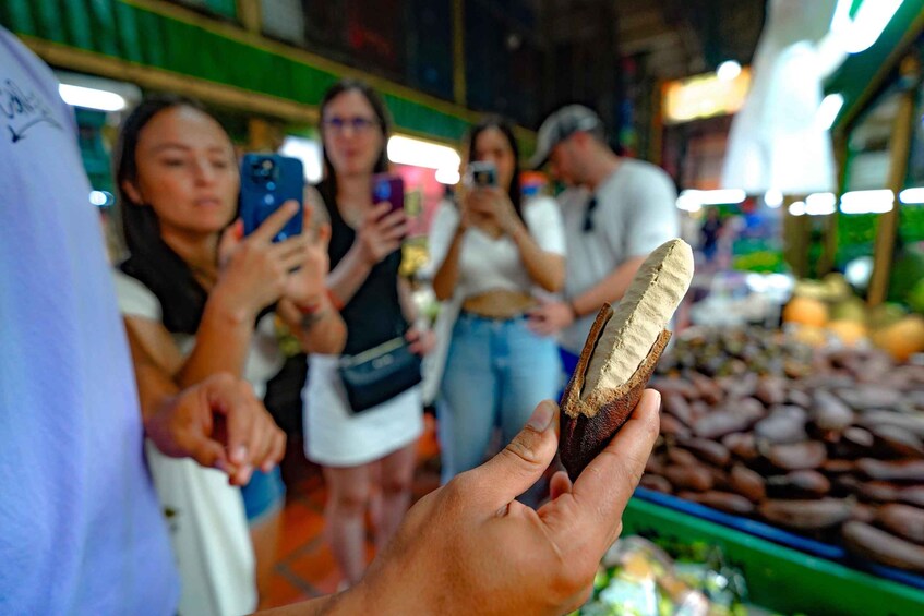 A person holding a piece of food at a market with other people taking photos. 4