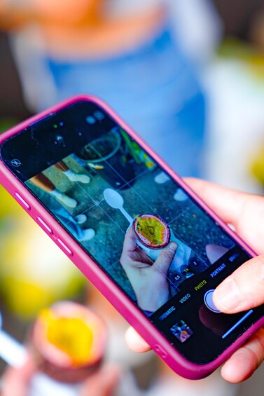 A hand holding a smartphone with a camera app open, displaying a photo of a half-eaten passion fruit. 3