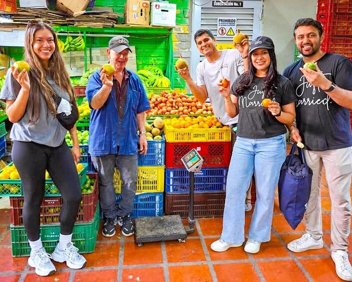 A group of people standing in front of a fruit market with crates of fruits and a weighing scale. 5