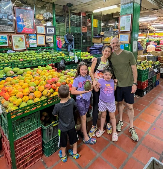 Eine Familie auf einem Obstmarkt, wo verschiedene Früchte in Kisten präsentiert werden. 1