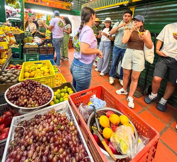 A market with people shopping and a woman standing in front of a display of grapes and oranges. 1