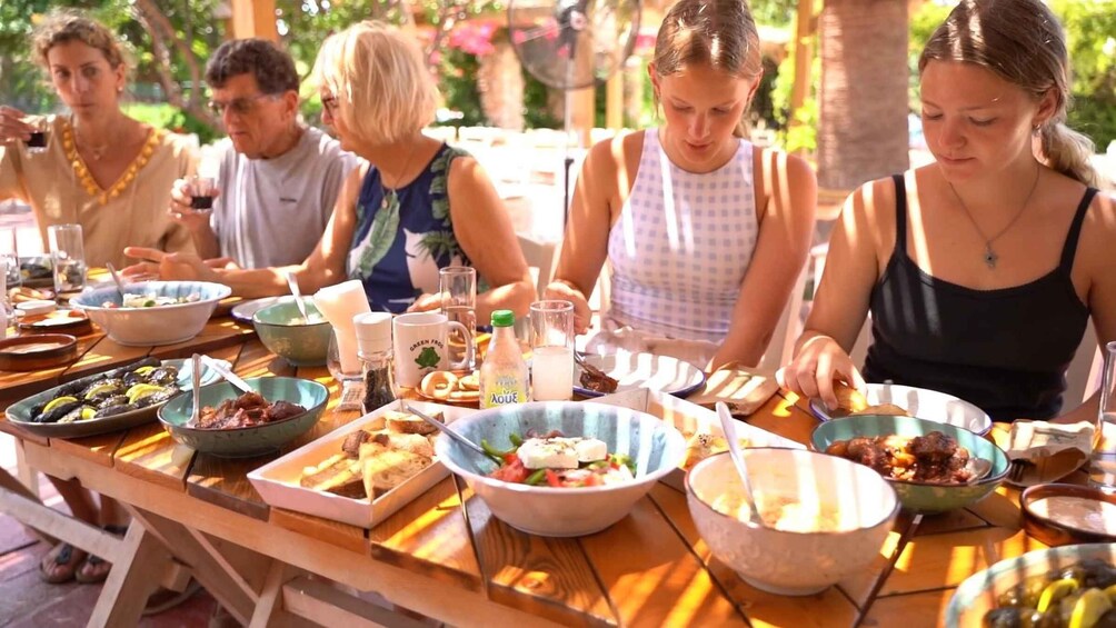 A group of people dining outdoors at a wooden table with various dishes and drinks. 1