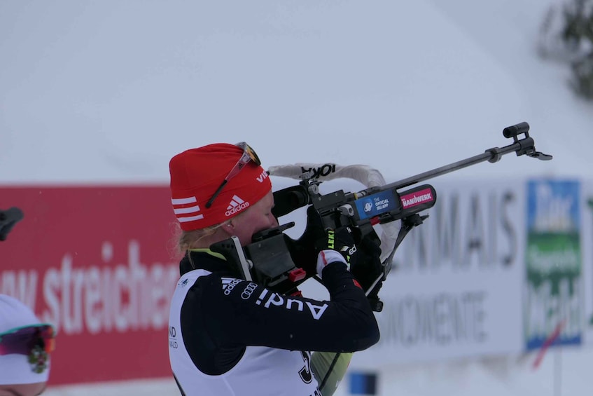 A person skiing with a rifle, wearing a red cap and black and white ski suit, in a snowy environment with a blurred background. 2