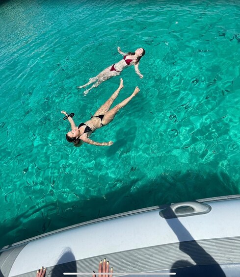 Two people floating on a turquoise body of water, likely a pool, with a boat in the foreground. 4