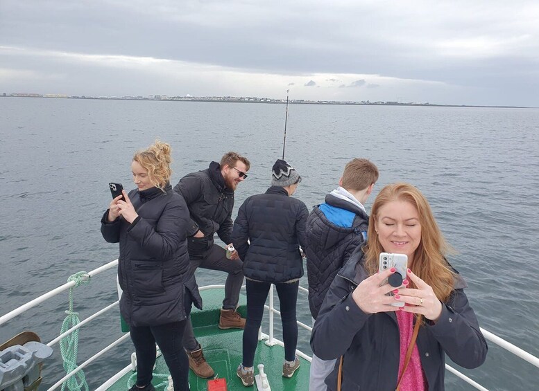 A group of people on a boat, some holding smartphones, with a cloudy sky and calm water in the background. 2