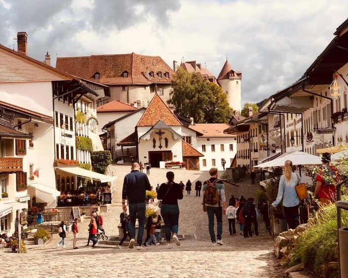 A cobblestone street in a historic town with people walking, shops, and traditional buildings. 1