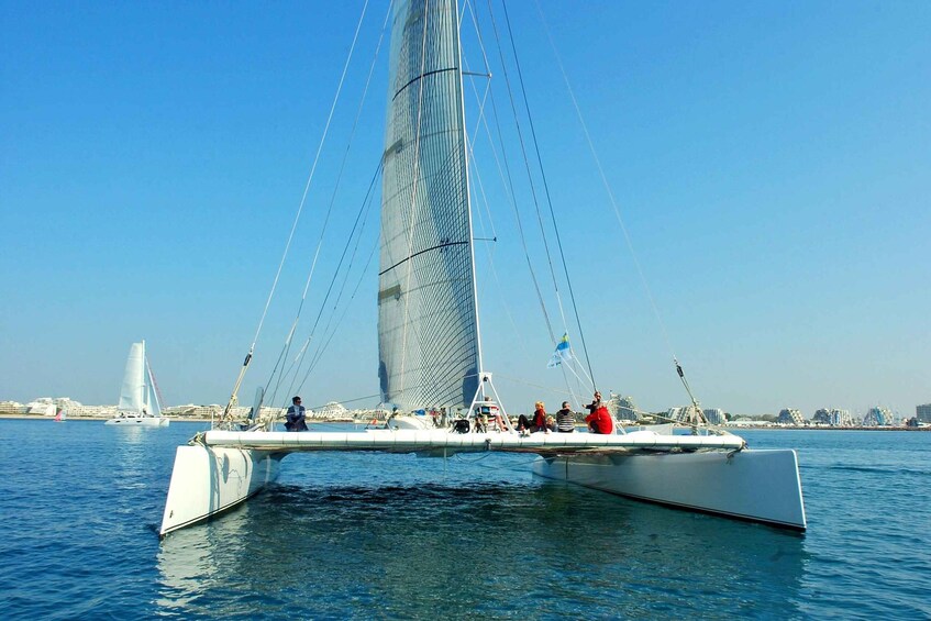 A sailboat with passengers on a calm sea, a large sail, and a distant cityscape with modern buildings. 2