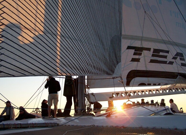 A sailboat with the word 'TEA' on its side, people on deck, and the sun setting in the background. 4