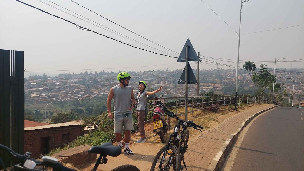 Two people on a hill overlooking a cityscape, with a road and a motorcycle in the foreground. 5